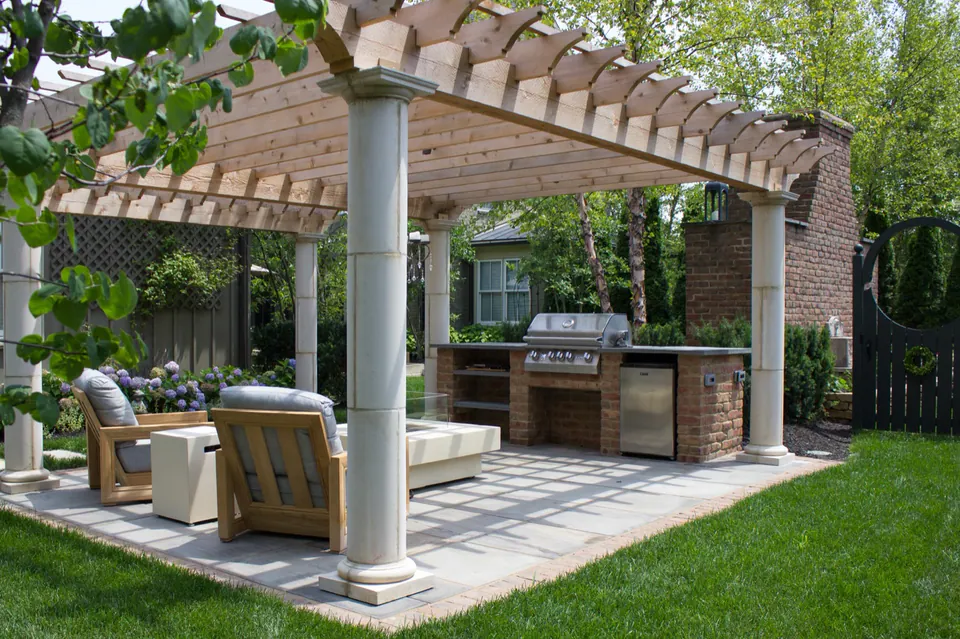 Outdoor kitchen patio under a white pergola with masonry columns